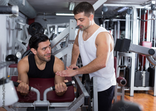 Man helping friend on fitness machine in gym