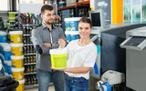 Young woman standing near man and holding bucket of paint in household store