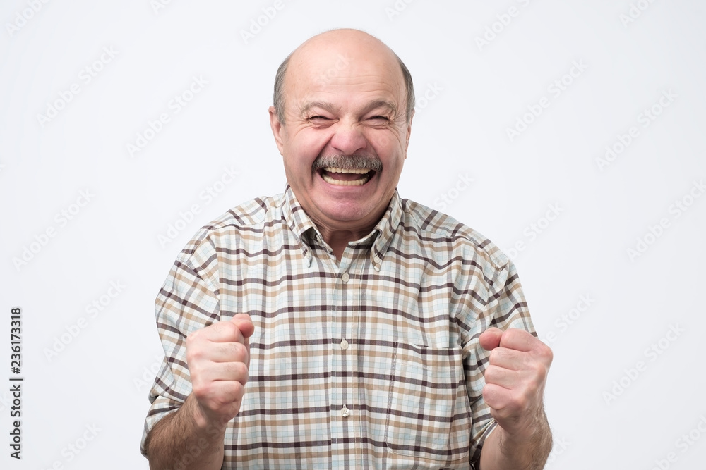 Naklejka premium Senior handsome man laughing and looking at camera with a big grin. He is so happy to find out about his pension savings
