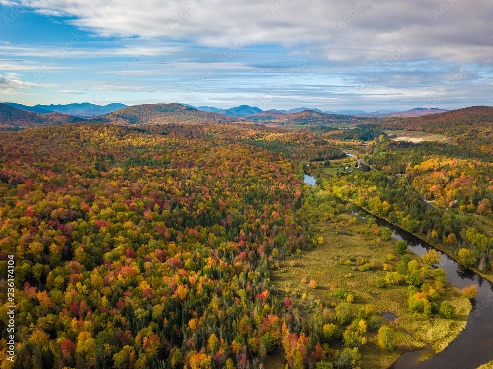 Low level aerial photograph featuring fall foliage in the Adirondack Park of New York State featuring peak fall foliage colors near Saranac Lake, NY and the Saranac River.