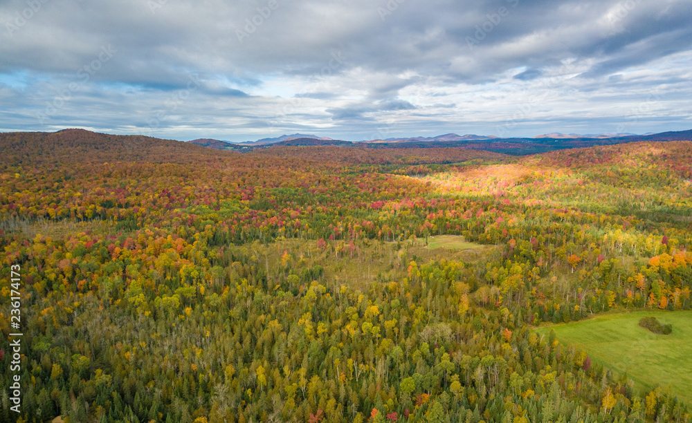 Low level aerial photograph featuring fall foliage in the Adirondack Park of New York State featuring peak fall foliage colors near Saranac Lake, NY and the Saranac River.