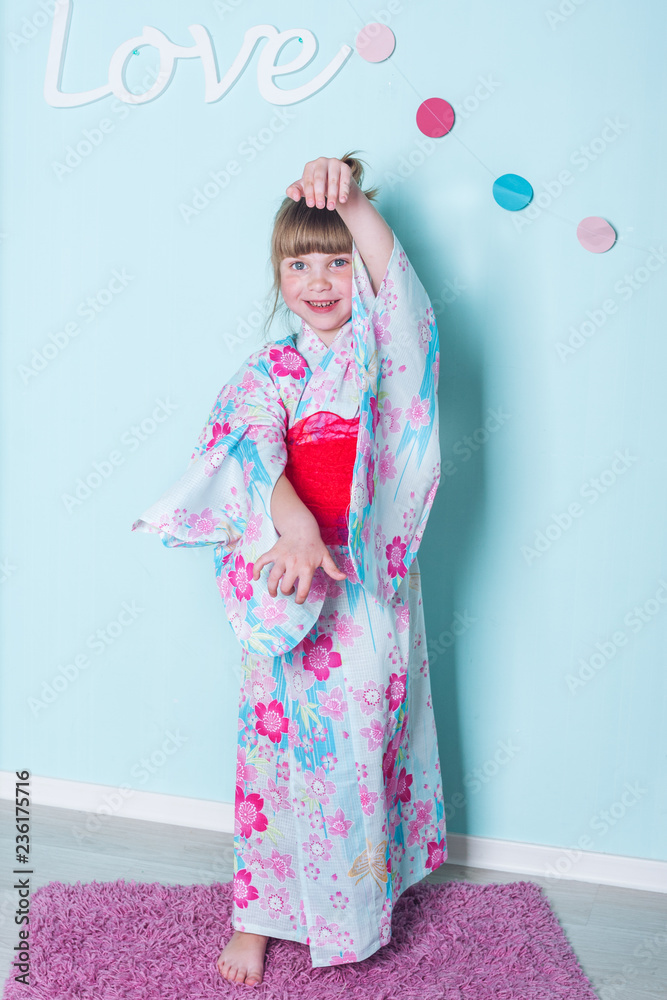 8 years old caucasian girl demonstrates japanese blue pink with flowers kimono, claps her hands, dance  