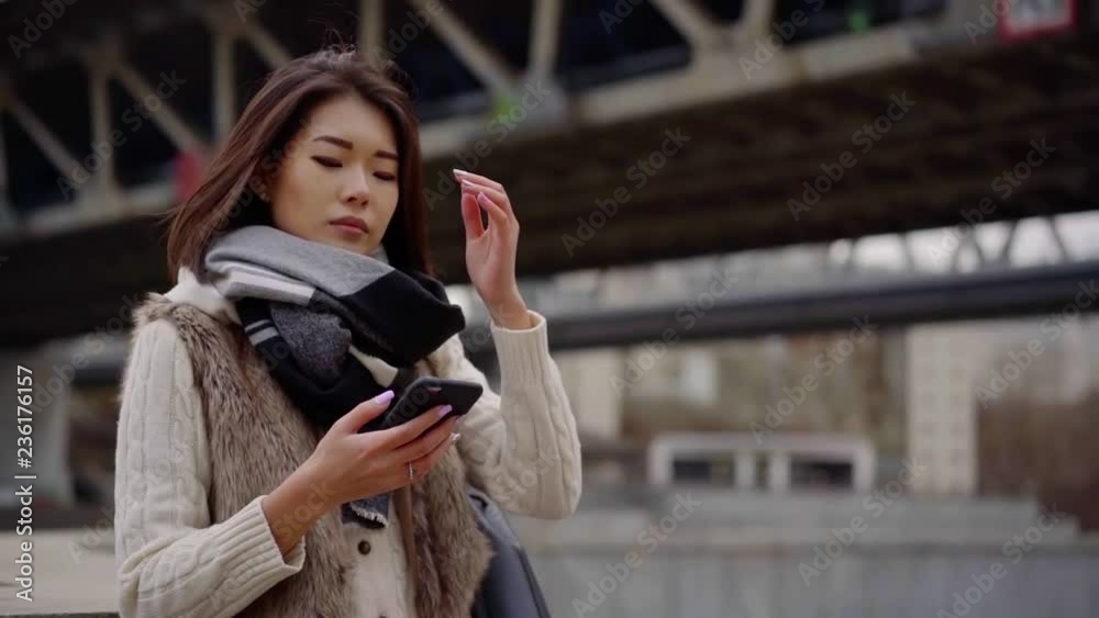 pretty asian girl is browsing by mobile phone with wireless internet, standing outdoors in city pretty asian girl is browsing by mobile phone with wireless internet, standing outdoors in city