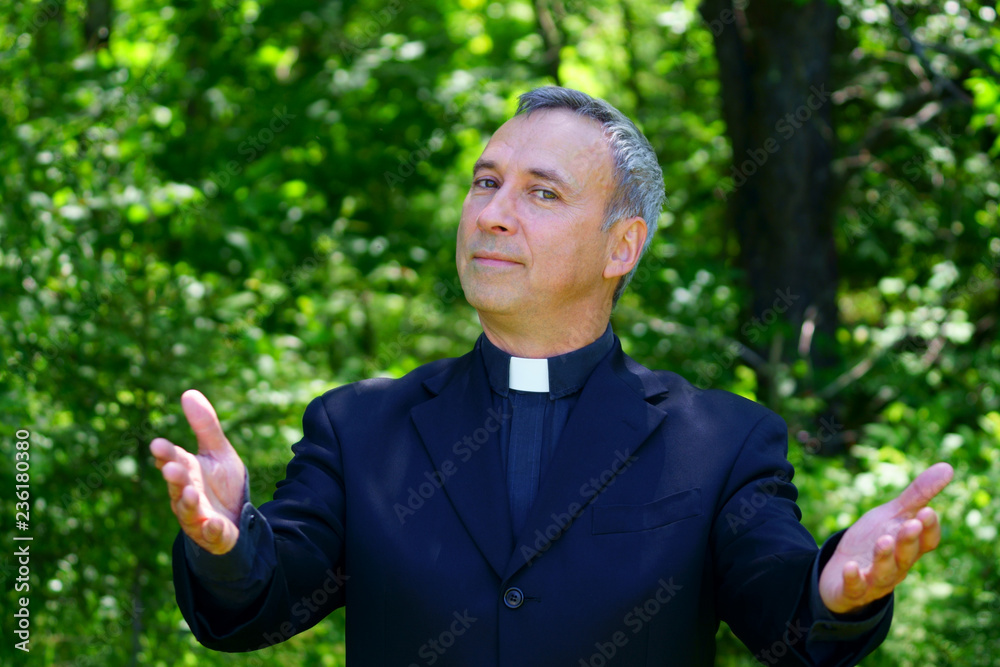 A good looking catholic priest is walking in the forest. Standing and looking at us with confidence, openning his arms. A good looking catholic priest is walking in the forest. Standing and looking at us with confidence, openning his arms.