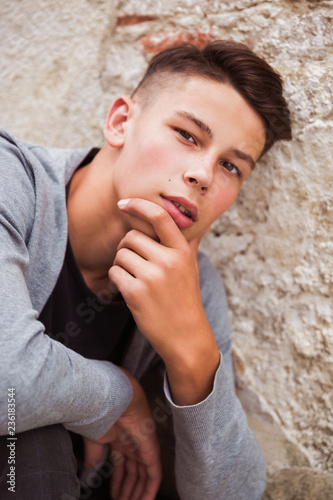 Portrait of the handsome young man who is sitting outdoor near the old house wall © Myroslava