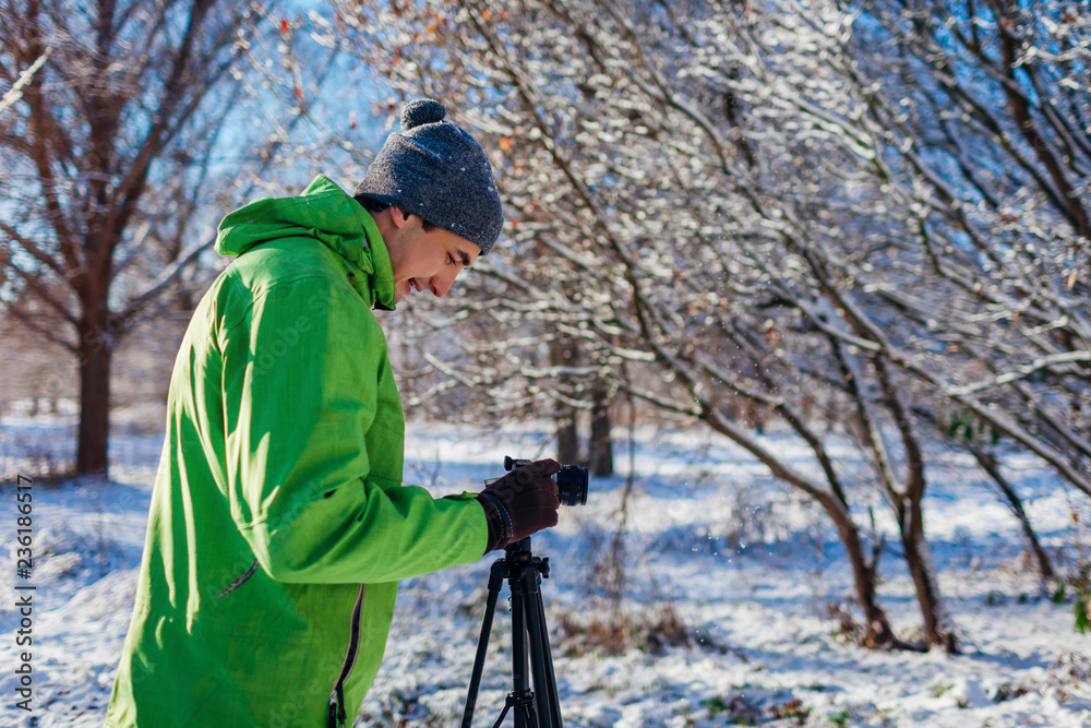Young photographer takes pictures of winter forest using camera and tripod
