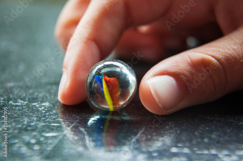 Child's fingers holding a glass marble on a black table