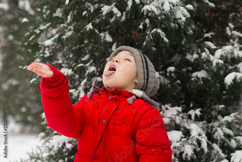 The child catches snowflakes on the tongue. The boy catches snow on the palm. Outdoor. Winter. Snow.