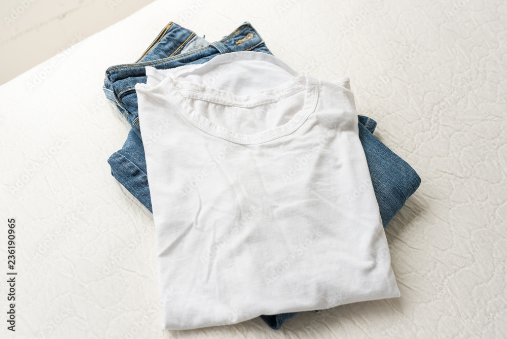 Fototapeta premium High angle view of folded plain white t-shirt and blue jeans on cream coloured bedding (selective focus)