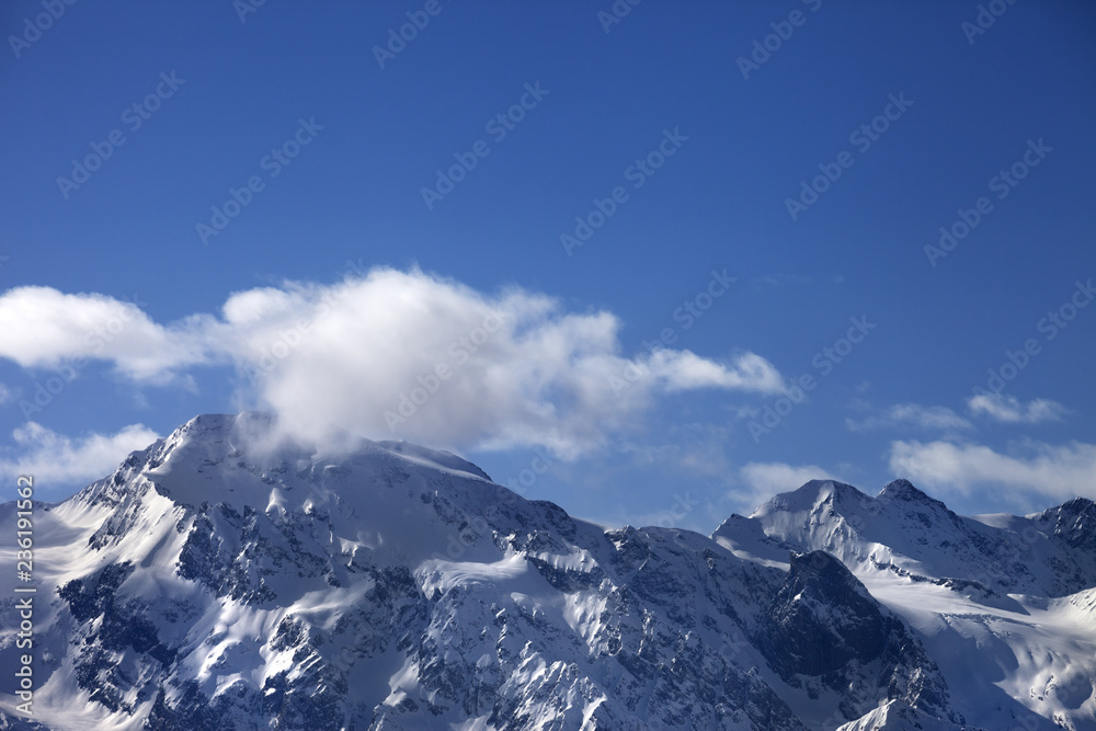 Snowy mountains with glacier and cloudy blue sky at sunny evening