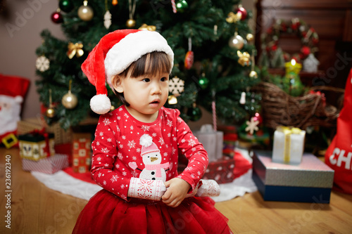 toddler baby girl wearing santa claus costume play in front of christmas tree