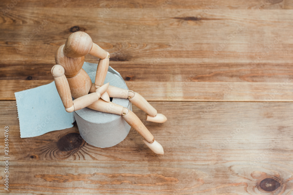 Wooden figure sit on a roll of toilet paper. Concept of the problem with digestion.