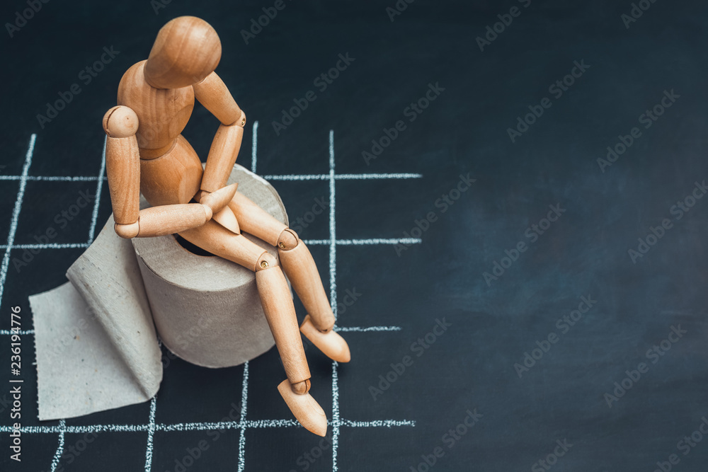 Wooden figure sit on a roll of toilet paper. Concept of the problem with digestion.
