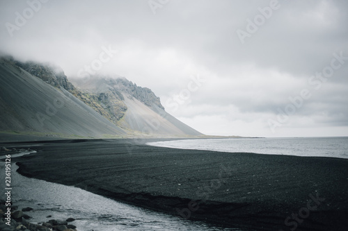 Epic and impressive landscape of cold and grey volcanic beach with black sand, mountains with green moss in background. Iceland or Greenland exploration expedition