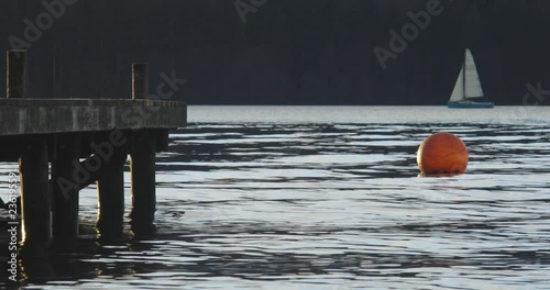 Buoy bobbing up and down in water, with boat sailing past dock in background. Windermere, Cumbria, UK. 4k