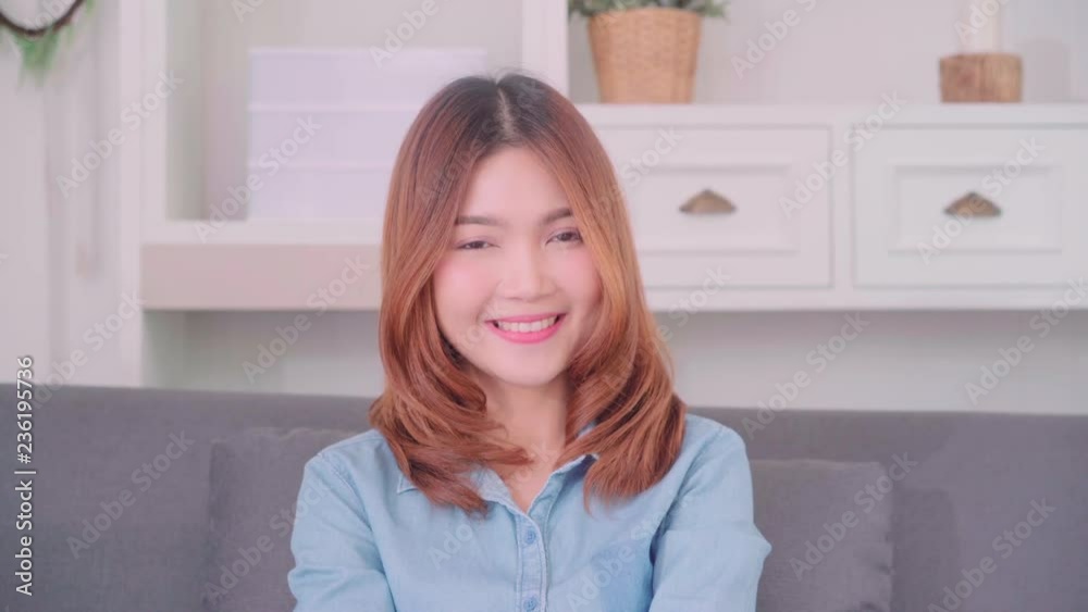 Teenager Asian woman feeling happy smiling and looking to camera while relax in her living room at home. Beautiful Asian young female using relax time at home concept. Teenager Asian woman feeling happy smiling and looking to camera while relax in her living room at home. Beautiful Asian young female using relax time at home concept.