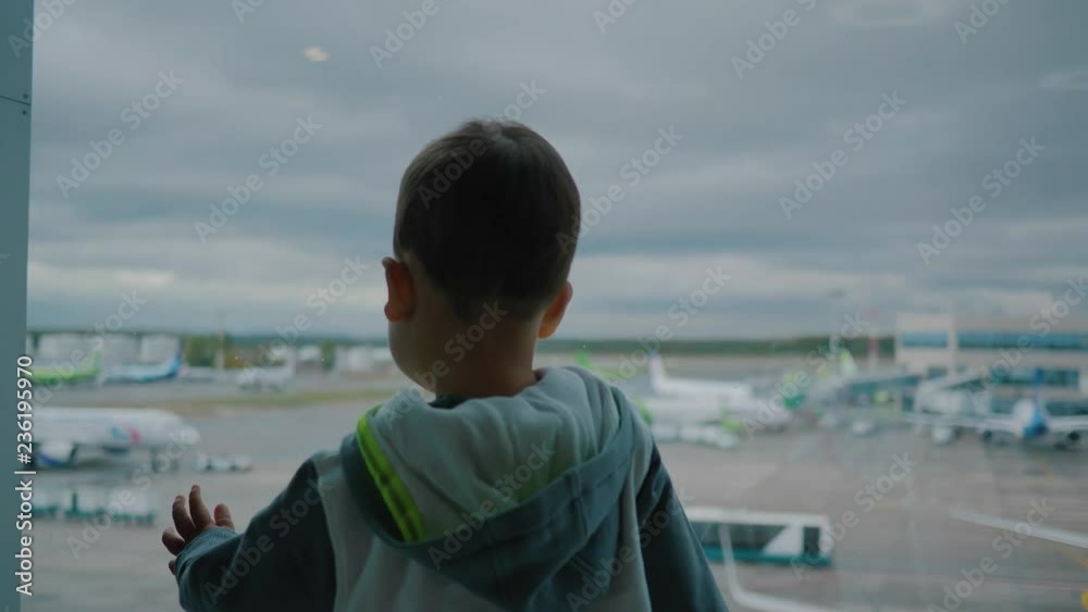 Little boy in airport looks on support vehicles and cloudy sky through window Little boy in airport looks on support vehicles and cloudy sky through window