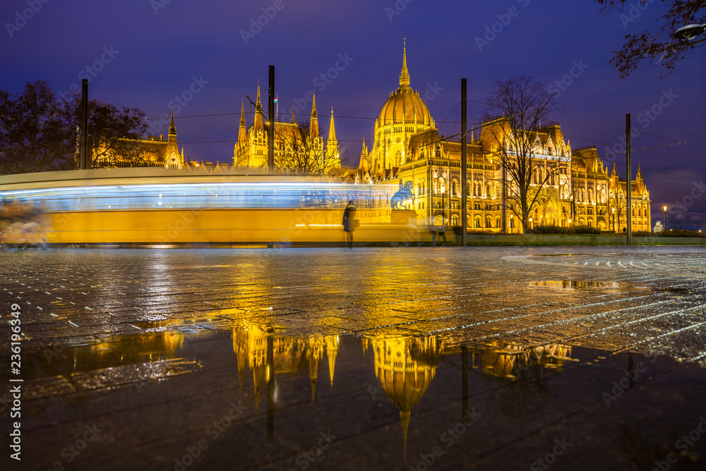 Budapest, Hungary - Illuminated Parliament of Hungary at blue hour with reflection and traditional yellow tram on the move