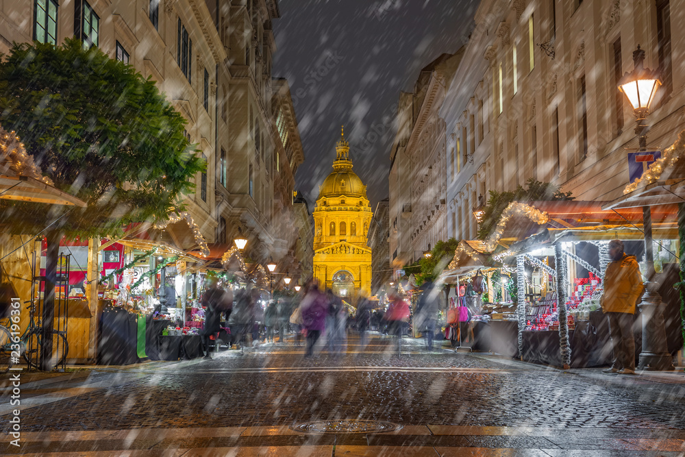Budapest, Hungary - Snowy night at Zrinyi street with Christmas market and illuminated St.Stephen's Basilica at background