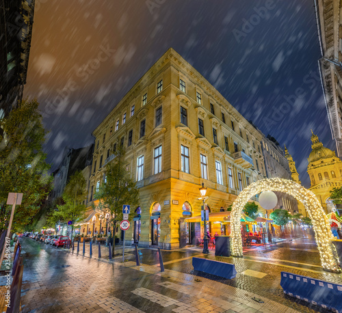 Budapest, Hungary - Snowy evening and Christmas market gate at the Zrinyi and Oktober 6 street corner with St.Stephen's Basilica at background photo