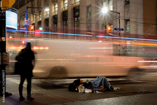 Editorial photo; Toronto, Ontario / Canada - November 13 2018: Homeless man on the streets of Toronto on a cold night with moving people and cars showing poverty in the city