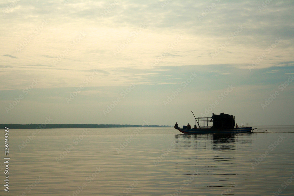 A fishing boat is silhouetted against the still, calm waters of Tonle Sap lake, in the village of Kampong Khleang near Siem Reap in Cambodia
