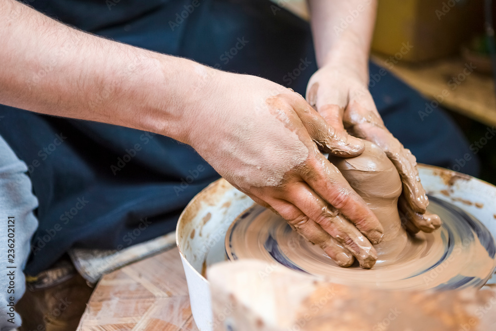 Professions Ideas and Concepts. Closeup of Hands of Male Potter Working with Clay Lump on Potter's Wheel in Workshop.