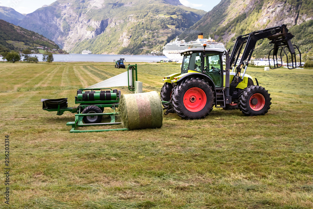 Small tractor with a round bale wrapper on a field in Geiranger, Norway. Small tractor with a round bale wrapper on a field in Geiranger, Norway.