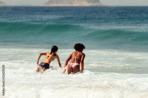 Two young women, one Caucasian and one African, jump on the sea break