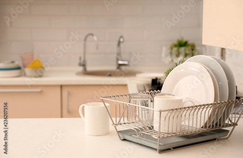 Dish drainer with clean dinnerware on table in kitchen. Space for text photo