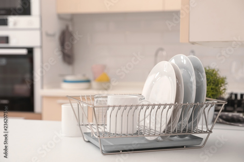 Dish drainer with clean dinnerware on table in kitchen photo