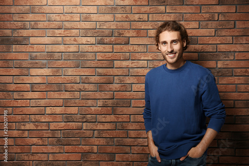 Handsome young man in warm sweater near brick wall. Space for text
