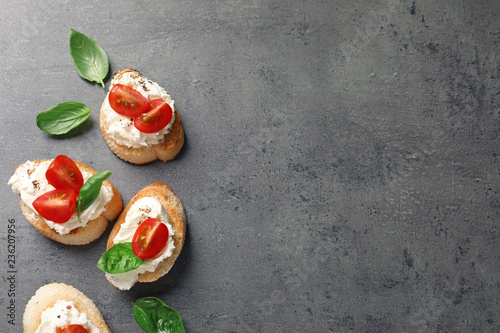 Pieces of baguette with tasty cream cheese and tomatoes on gray table, flat lay. Space for text
