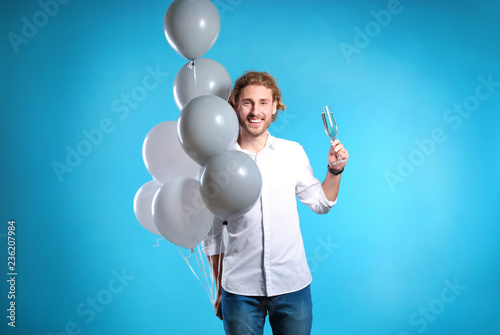 Portrait of happy man with champagne in glass and party balloons on color background