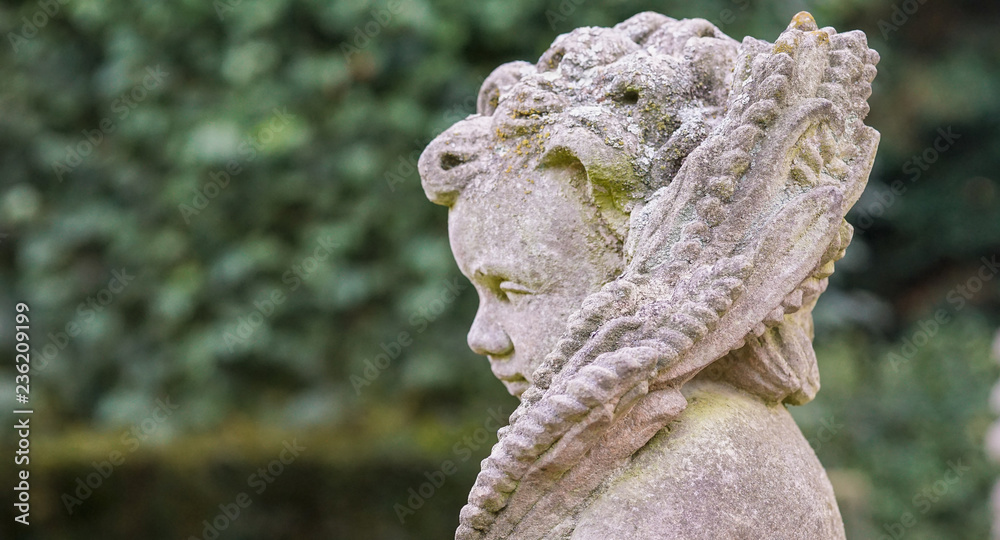 Stone angel statue in garden. Guardian angel statue in sunlight as a symbol of love in garden. Stone angel statue in garden. Guardian angel statue in sunlight as a symbol of love in garden.