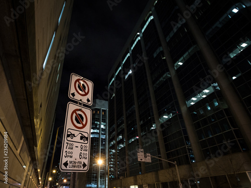 Typical North American paking and no parking signs with detailed instructions on the parking regulations taken at night in Ottawa CBD, Ontario, Canada, with a sign indicating bus lanes behind