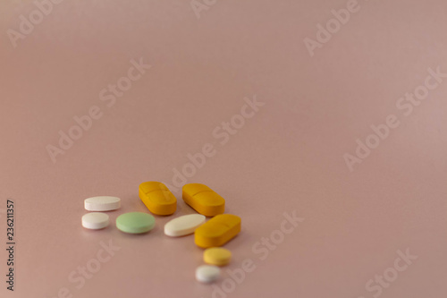 Medicines of different sizes and colors on a neutral pink background.