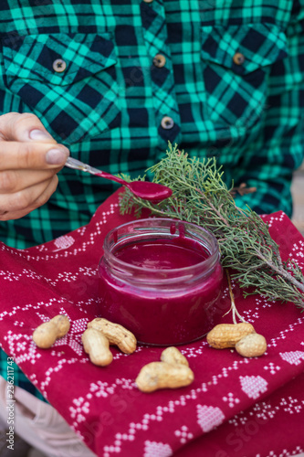 Woman hands holds, takes with spoon red homemade tomato, beetroot sauce dip with peanuts, nuts in jar used for dressing the salads. Vegan vegetarian healthy food