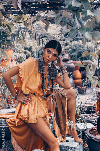 beautiful young fashionable woman with make up and stylish boho accessories posing on natural tropical background