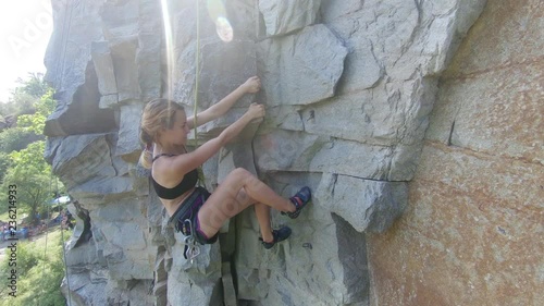 young girl climbing a rock with climbing equipment