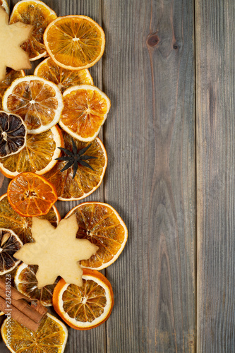 Dry slices of orange with cookie, star anise, cinnamon, on brown wooden background, top view, vertical composition