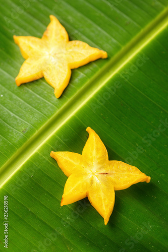 Slices of ripe yellow star fruit carambola or star apple ( starfruit ) on green banana leaf, vertical composition