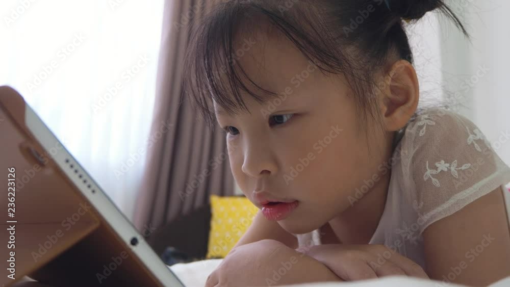 Little asian girl lying on bed ,watching cartoon online via tablet computer at home Stock ビデオ | Adobe Stock