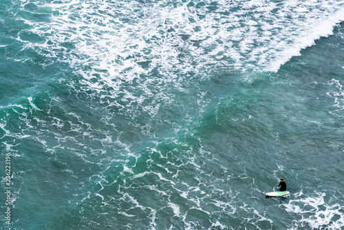 Aerial view of a surfer in the middle of the pattern create by the foam of a wave. Piha black sand beach New Zealand