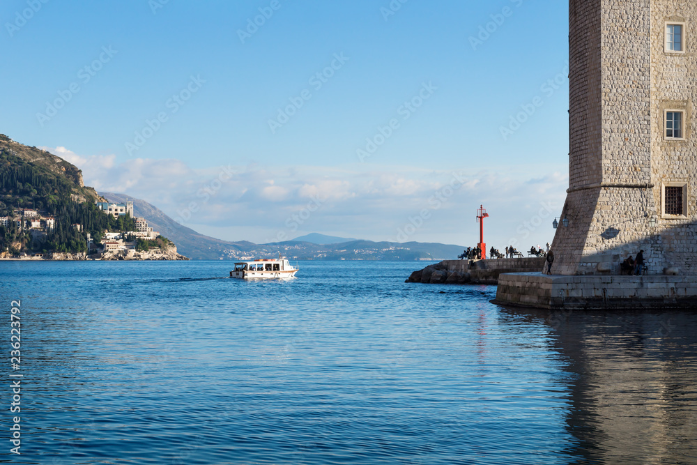 Boat leaving the harbor of Dubrovnik with wall of fortress and lighthouse in winter, Croatia