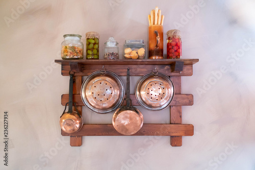 Copper utensils hanging on the shelf: colander, dipper, frying pan, jars, cutting board. Copperwares hanging on the wall.