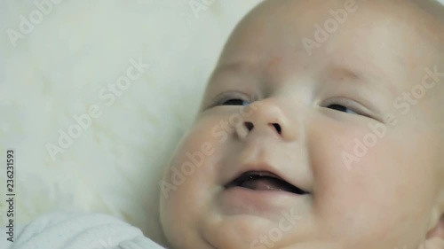 Close-up of a happy five-month baby lying peacefully on a white blanket and smiling