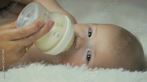 Mom feeds her newborn baby with milk while lying on a white blanket in slow motion.