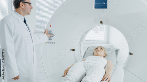 In Medical Laboratory Radiologist Controls MRI or CT or PET Scan with Female Patient Undergoing Procedure. High-Tech Modern Medical Equipment.