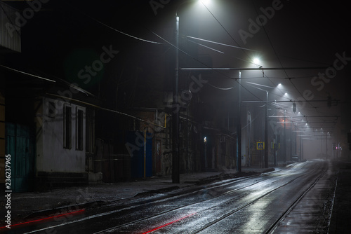 Street lights foggy misty night. Tram route on a city street.